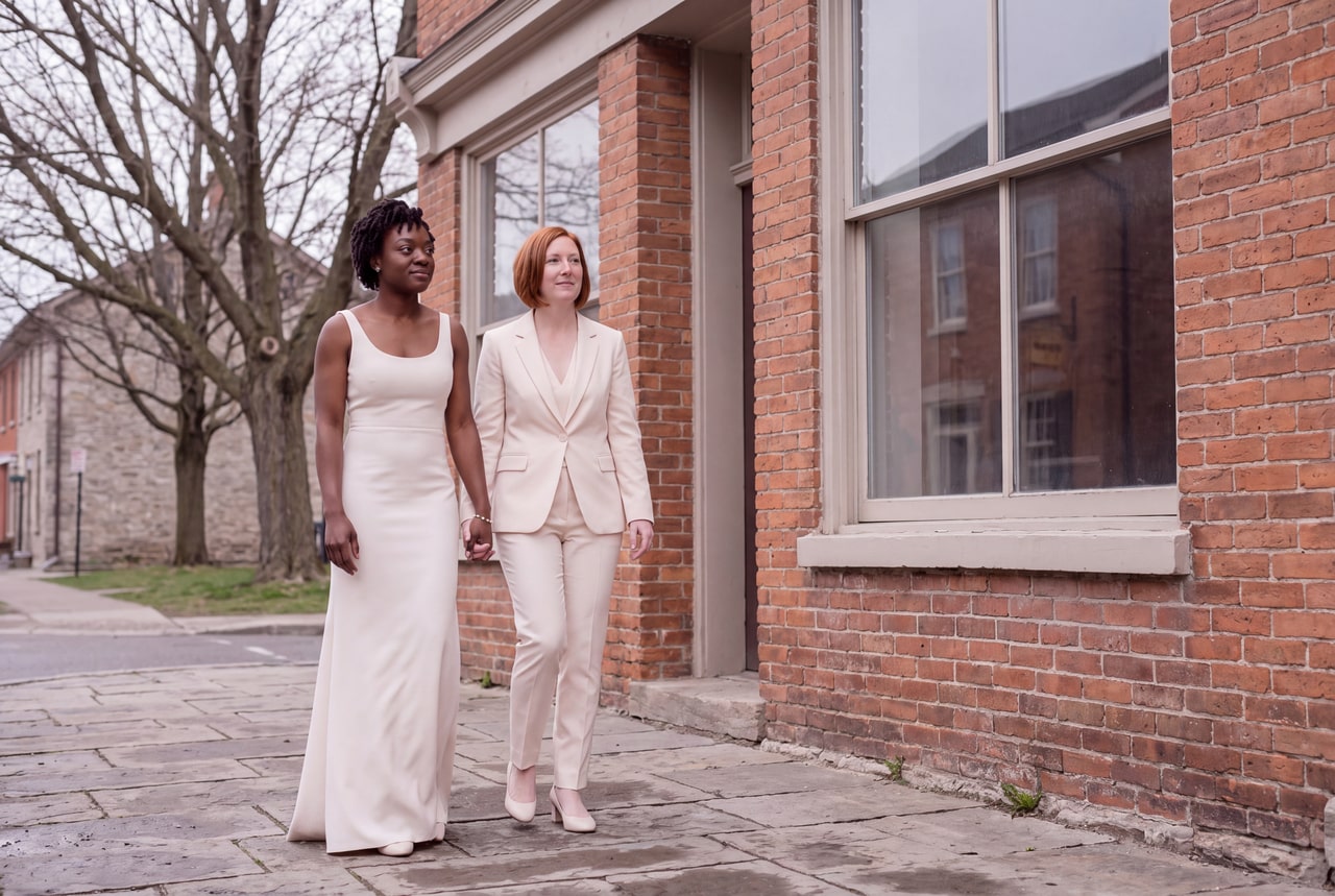Two brides taking a quiet walk beside brick buildings on an old-town street
