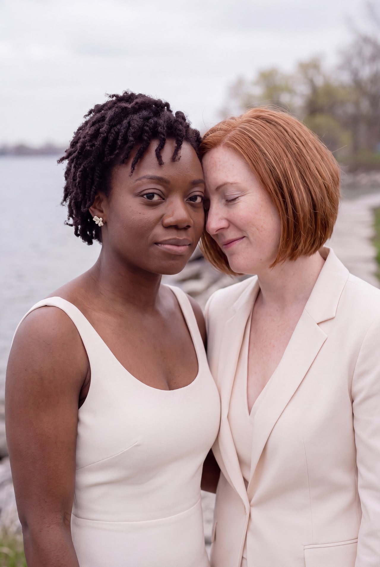A close portrait of two brides leaning their heads together beside the lake