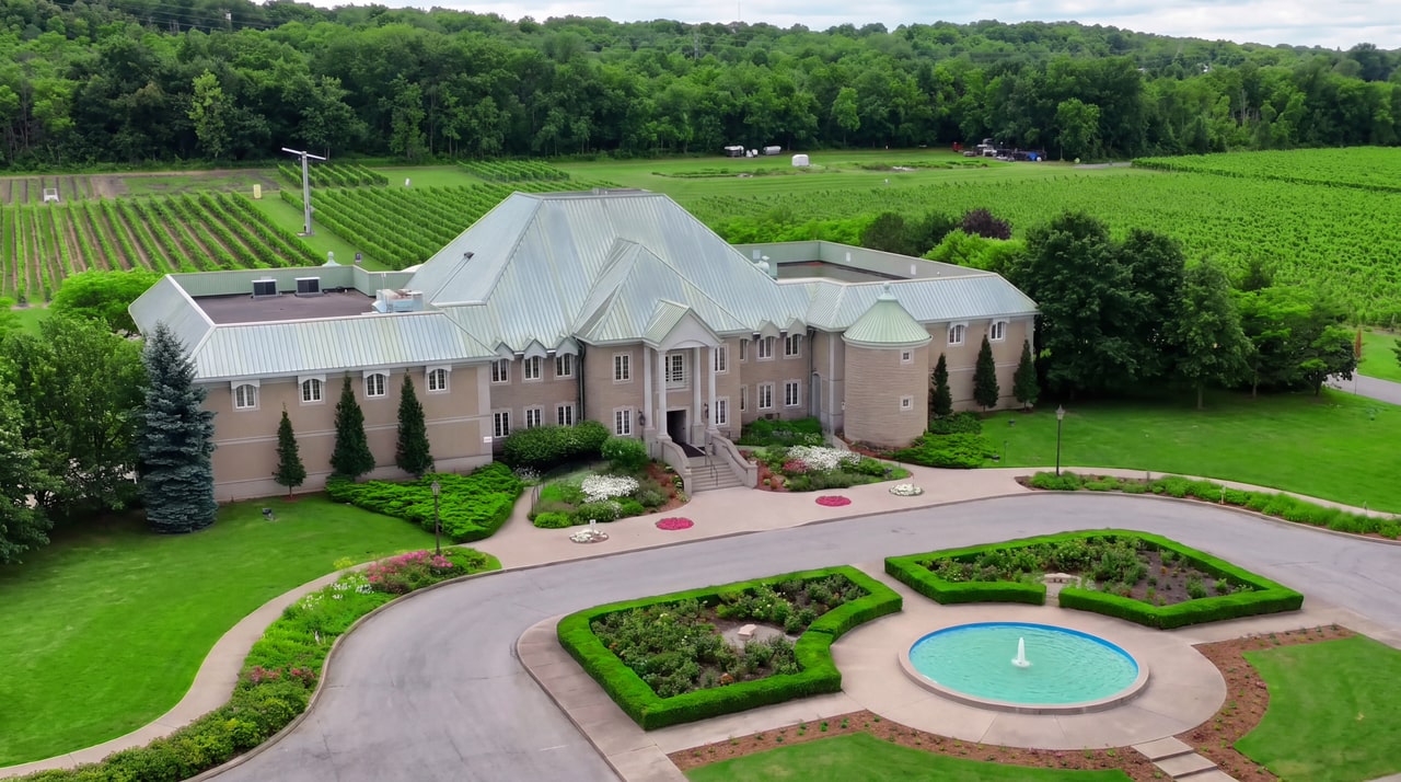 Elevated view of Château des Charmes, with a pale stone facade, turret and landscaped fountain courtyard.