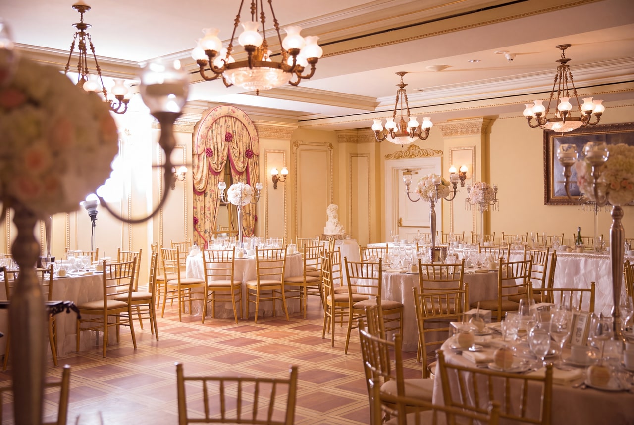 Cream-and-gold reception room with chandeliers, a draped arch and white floral table arrangements at Prince of Wales.