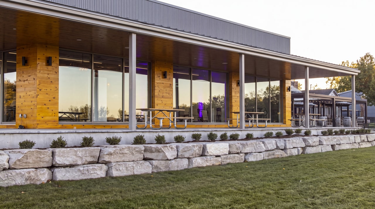Glass-fronted Event Centre terrace at Ravine Vineyard, with timber piers and a low limestone garden wall.
