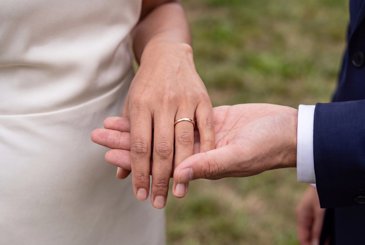 A gold wedding band already seated on the bride’s finger as her hand rests in the groom’s open palm